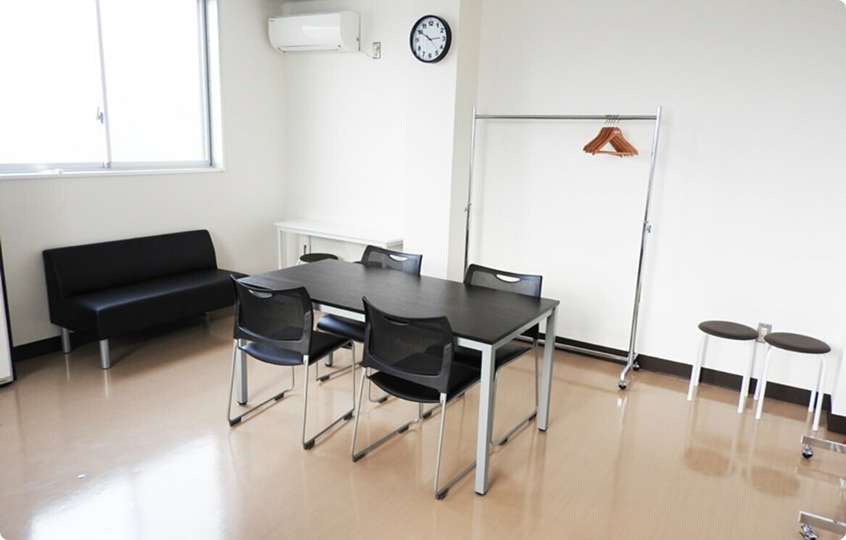 楽屋の様子。テーブルと椅子、ソファ、ハンガーラックとハンガー