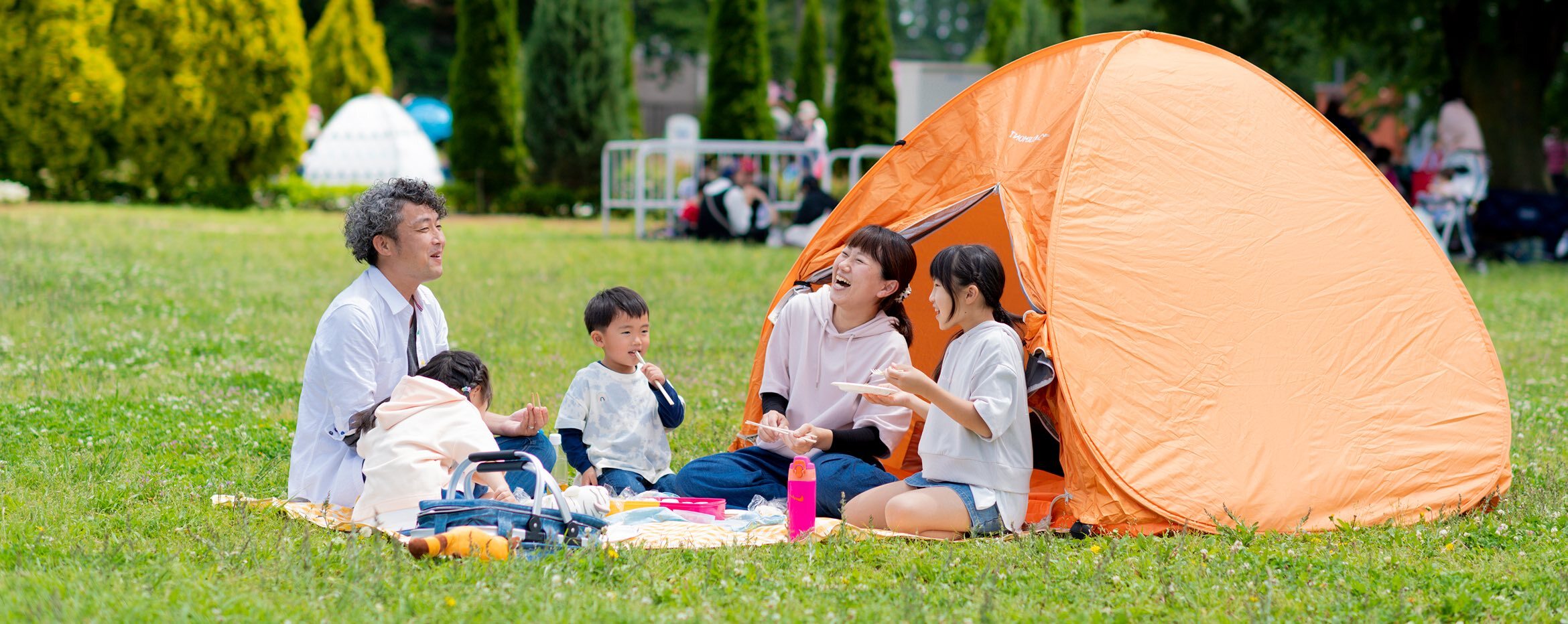家族が広場で楽しそうにお弁当を食べている様子